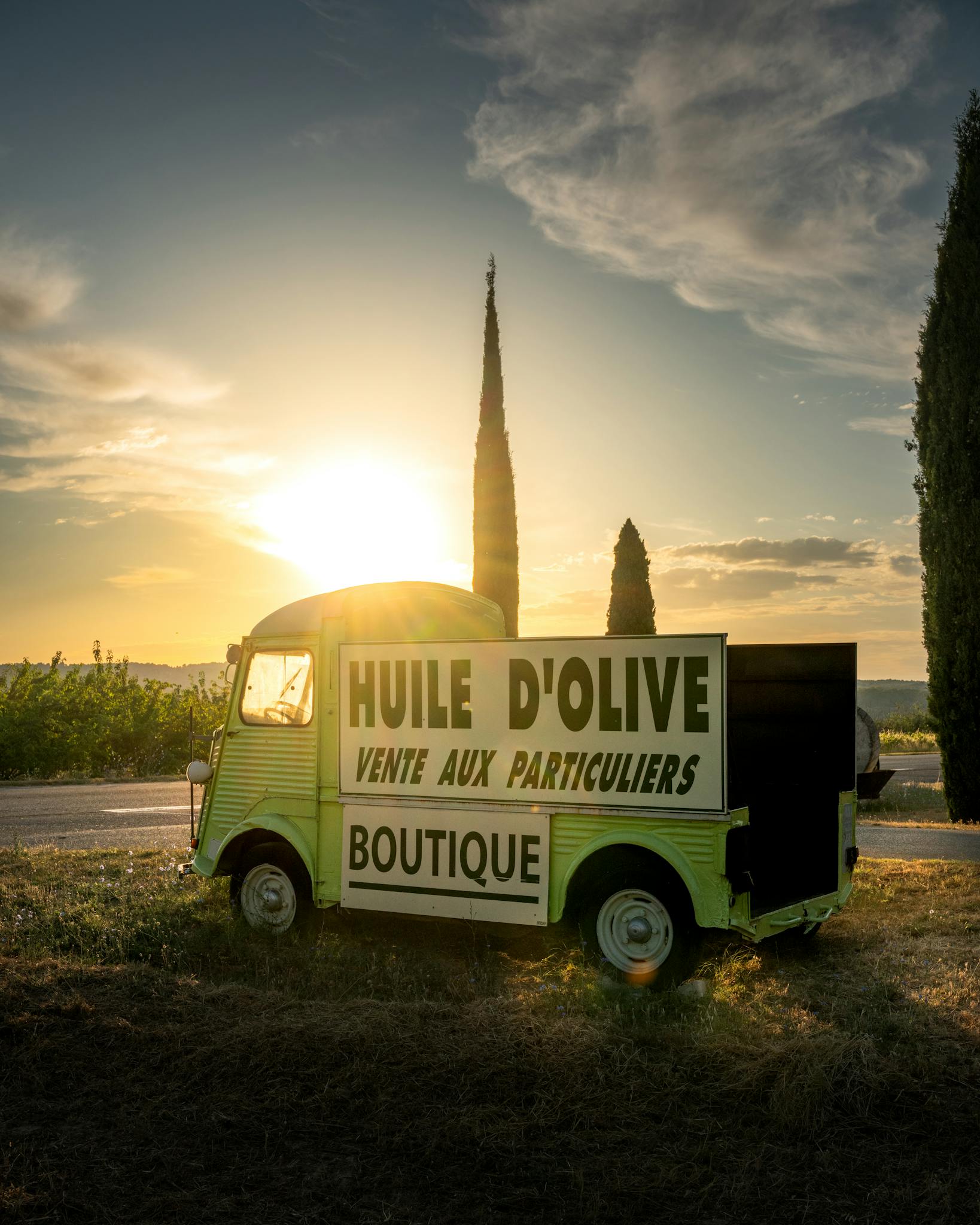 Vintage olive oil truck in Provence with sunrise backdrop and cypress trees.